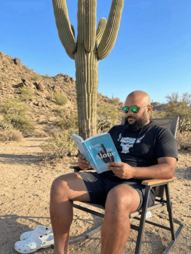 Rho reading in a chair beneath a saguaro in the Sonoran desert